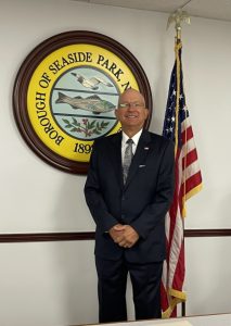 Council President Marty Wilk Jr. standing in front of the American Flag and the Borough Seal